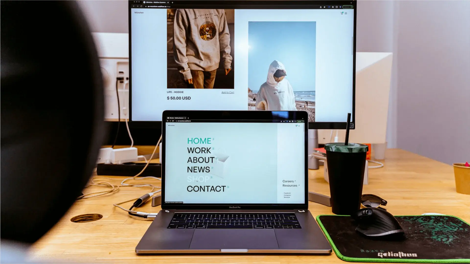 Miejsce pracy z dwoma monitorami, z których jeden wyświetla stronę internetową z odzieżą, a drugi stronę internetową.